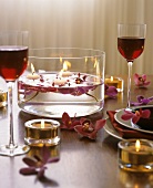 Schale mit Blüten und Kerzen auf romantisch gedecktem Tisch
