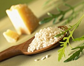 Risotto rice on a wooden spoon; rocket and piece of parmesan