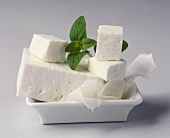 Sheep's cheese with a piece cut off and basil in a bowl