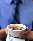 Man holding small bowl of tomato & orange soup with shrimps