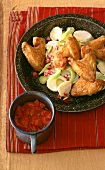 Chicken wings on potato salad and mug of tomato sauce