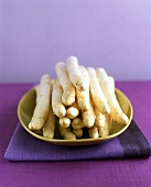 White asparagus spears on yellow plate, purple background
