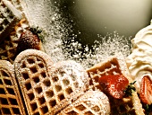 Waffles with icing sugar, decorated with strawberries & cream