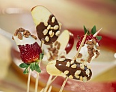 Chocolate-coated fruit with puffed rice on sticks