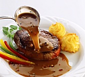 Pouring pepper sauce over beef steak
