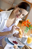 Young woman at breakfast table eating croissant