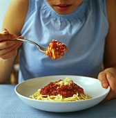 Young woman eating spaghetti with tomato sauce