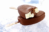 Two vanilla and chocolate ices on sticks, one with a bite taken