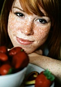 Freckled woman in front of a bowl of strawberries