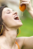 Frau lässt Saft einer frischen Orange in ihren Mund tropfen
