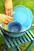 Geschirr abwaschen in blauer Schüssel auf Campinghocker