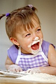 Small laughing girl baking with flour on her face