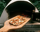 Pizza on wooden paddle in front of pizza oven