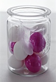 Lila und weiße Eier mit Federn im Glas