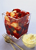 Red fruit salad in glass and a bowl of whipped cream