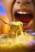 Pasta on fork, person with mouth open behind