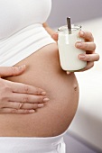 Schwangere hält ein Glas Naturjoghurt vor den Bauch (Detail)