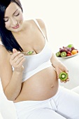 Sitzende schwangere Frau, eine Kiwi essend