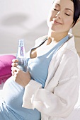 Sitzende schwangere Frau, Flasche Mineralwasser in der Hand