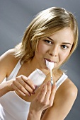 Young woman with yoghurt jar, spoon in mouth