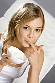 Young woman with bowl of yoghurt, licking her finger