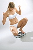 Young woman, squatting on scales, looking triumphant