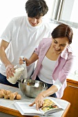 Young couple baking, with mixing bowl, hand blender & cookbook