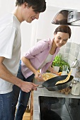 Man at cooker tossing pancake, woman standing beside him