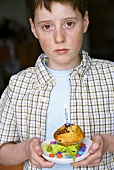 Junge hält Muffin mit brenneder Kerze
