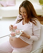 Schwangere Frau isst herzförmige Petit fours (Gebäck)