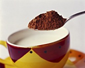 Cocoa powder being spooned into a cup of milk