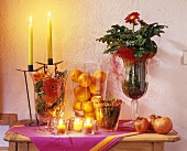 Candles & tea lights beside fruit in glasses & potted gerbera
