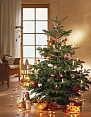 Decorated Christmas tree with presents and row of tea lights on parquet flooring
