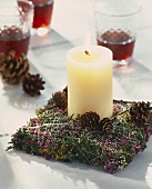 Burning candle on bed of heather and moss with fir cones