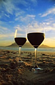 Red wine glasses on beach with mountain backdrop, S. Africa