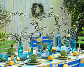 Gedeckter Tisch mit blauen Flaschen, Olivenzweigen und Zitronen