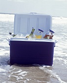 Coolbox with drinks bottles, juice cans, & glasses in sea