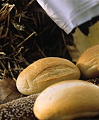 Mehrere helle Brötchen & dunkles Sesambaguette auf Stroh