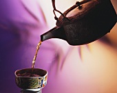 Tea being poured from a teapot into an Asian bowl