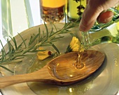Pouring olive oil out of jug onto wooden spoon on plate