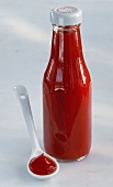 Tomato ketchup in a bottle and beside it on white spoon