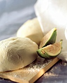 Yeast dough sprinkled with flour on board with fig slices