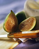 Fresh halved figs on cloth on wooden board with knife