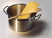 Kochtopf mit Spaghetti und Holzgabel auf hellem Untergrund