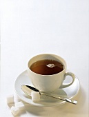 Tea in white cup; sugar cube on spoon and beside cup