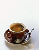 Espresso in brown cup; spoon with sugar in saucer