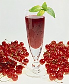 Cherry juice in glass with mint leaf, surrounded by cherries
