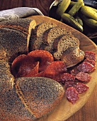 Poppy seed and aniseed bread with salami on a wooden plate 
