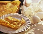 Pancake torte on plate & baking sheet; decoration: eggs, flour