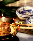 Gemüse mit Reis auf Stäbchen vor Wok und asiatischen Schalen